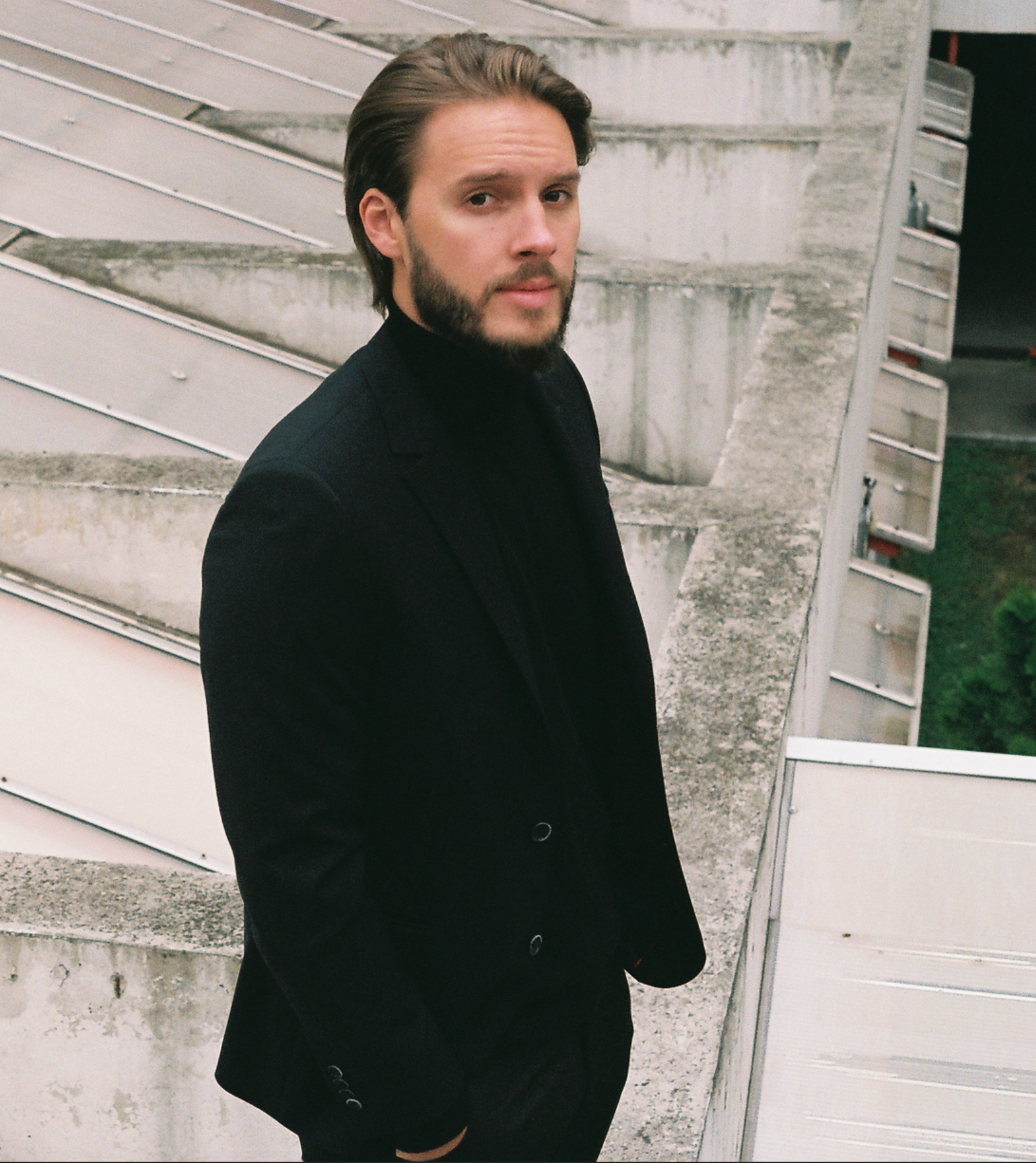 Danilo wearing a black jacket and turtleneck against concrete architecture